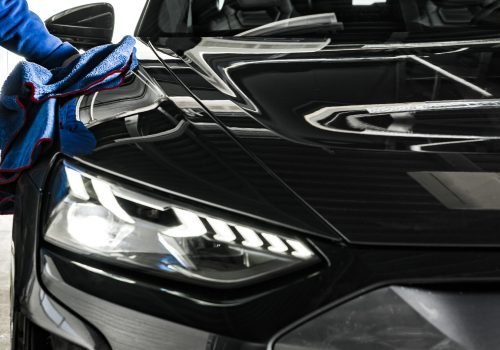 Professional Car Wash and Detailing Worker Cleaning Car Body with a a Soft Cloth. Automotive Industry Theme.