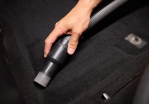 Hand-held vacuum being used to clean car interior, focusing on precise cleaning of nooks and corners.
