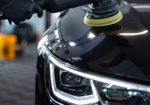 Professional man with polishing tool polishing black car in garage . Detailing. Varnish care and scratch removal