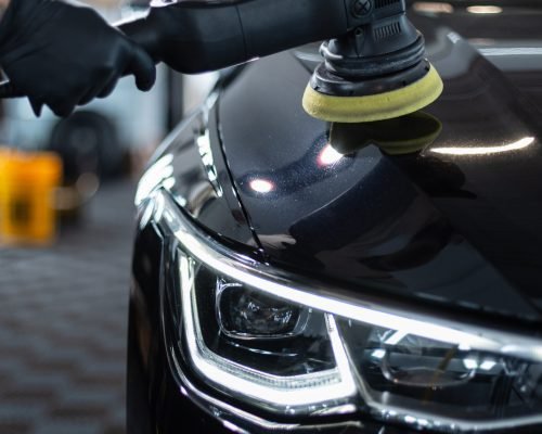 Professional man with polishing tool polishing black car in garage . Detailing. Varnish care and scratch removal