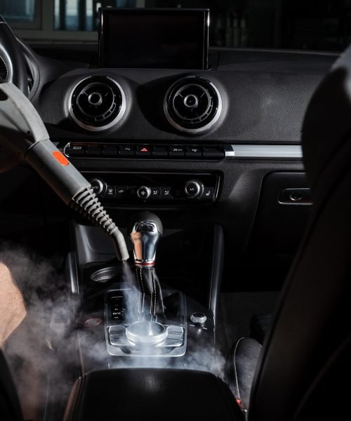 Steam cleaning of gearbox and dashboard in car. Vaping steam. Cleaning individual elements of black leather interior in auto. Creative advert for auto detailing service